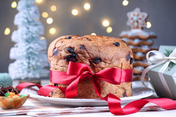 Tasty Christmas panettone cake decorated with red ribbon on table against blurred lights, closeup. Bokeh effect