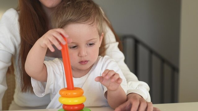 the child collects a toy pyramid. mom plays with son at home happy family. development of fine motor skills fun in a newborn child. happy family mom and baby play pyramid game. preschool education