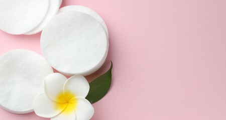 Clean cotton pads and plumeria flower on pink background, flat lay. Space for text