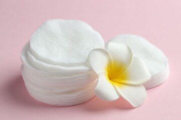 Clean cotton pads and plumeria flower on pink background, closeup