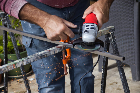 Close-up of the hands of a white Caucasian male holding an angle grinder without gloves to smooth the surface of a steel metal rod - home improvement health and safety do it yourself concept shot