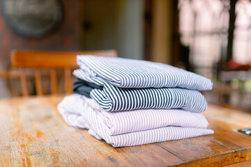 Freshly laundered stack of colorful striped shirts on rustic wooden table evokes a sense of cozy comfort and organized living, perfect for home and lifestyle projects