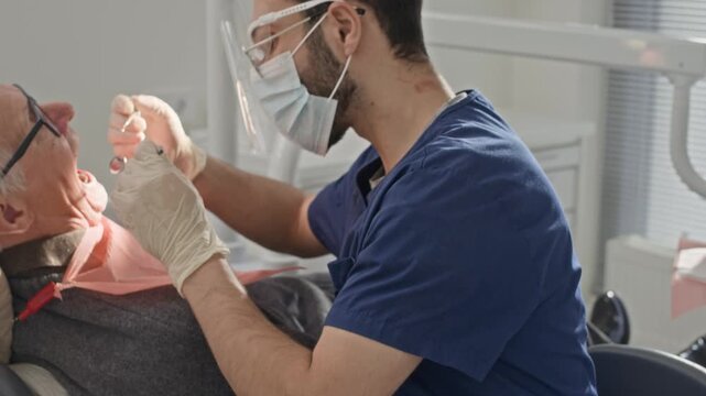 Dentist in scrubs and gloves providing oral care to elderly patient during treatment session in clean contemporary dental clinic