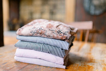 Stylish stack of folded shirts on rustic wood table creates a cozy, organized vibe for fashion blogs, minimalist lifestyle brands, and home organization content