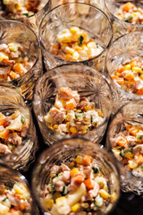 Multiple glass cups filled with a colorful mix of diced chicken, corn, carrots, cucumbers, and creamy dressing, served as individual appetizers. Ideal for catering