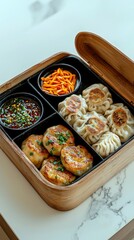 A bento box filled with various dumplings, shredded carrots, and a dipping sauce.