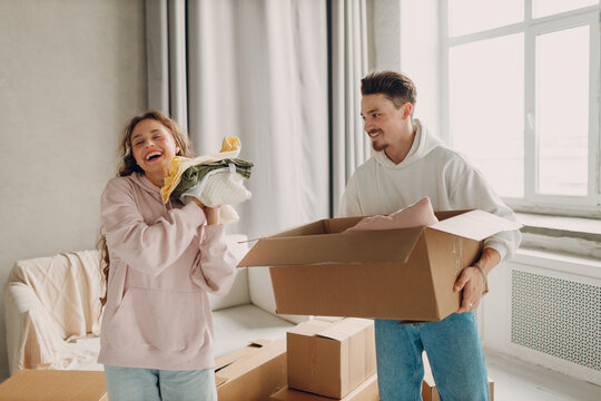 Happy young family couple man and woman unpacking box after moving cardboard boxes to new home apartment.