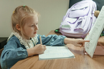 Young girl studying from a book and writing on a notebook at her desk. Child engaged in homework or homeschool. Education concept.