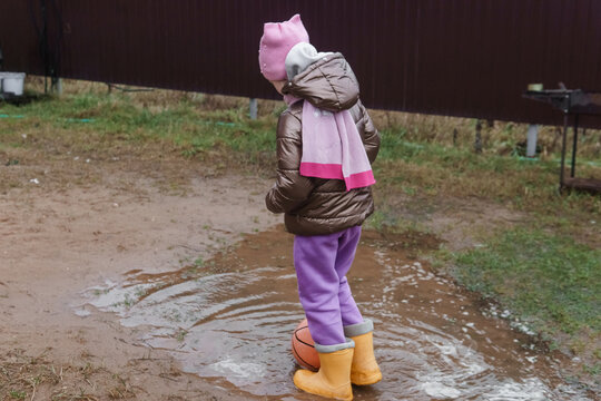 Kid is standing in a puddle with a ball. Childhood play and fun in rainy weather for children activity. Joyful outdoor recreation.