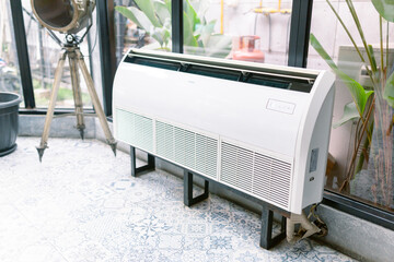 Modern white air conditioner in stylish sunlit room with vintage spotlight and patterned floor, perfect for cooling down a creative workspace or home office in summer