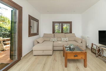 Front view of a country-style living room with a beige linen sofa, reclaimed wood coffee tables, and large windows overlooking the natural garden