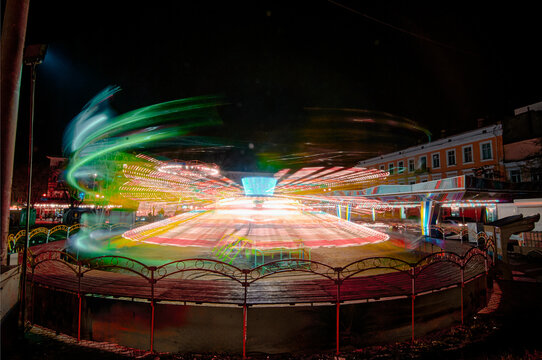 Bright, swirling neon lights form patterns as a carnival ride spins during nighttime, creating colorful trails that enhance the amusement and joy of the lively fair atmosphere under the dark sky.