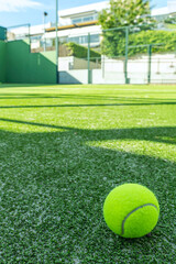 A tennis and padel court with a green artificial grass surface with a tennis ball in the corner