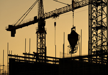 Constructing the Future, scene from the building site of upcoming modern high-rise building with crane and heavy machinery in silhouette