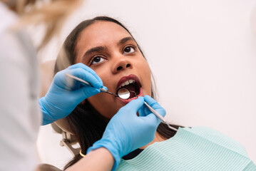 Close up of Dentist wearing blue gloves examining patient's teeth with dental tools in dental clinic