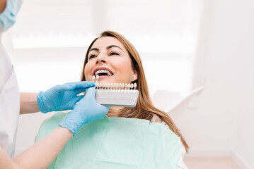 Dentist choosing right shade of teeth for female patient during whitening procedure in dental clinic