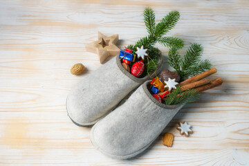 Felt slippers filled with sweets and Christmas decoration on a light wooden floor at Saint Nicholas...