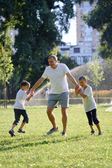 Obraz premium Father and his two young sons enjoying a playful moment together in a sunny green park. A display of joy and togetherness, perfect representation of family bonds during outdoor activities.