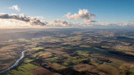 Aerial view of patchwork farmland with a winding river, rolling hills in the distance, and scattered farms under a blue sky. Concept Aerial farmland, Patchwork fields, Winding river, Rolling hills