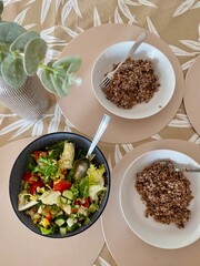 three plates of buckwheat porridge and salad on the table