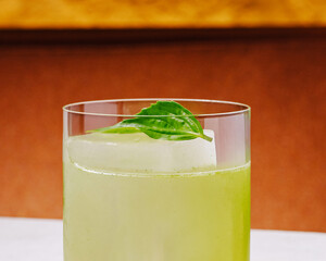 Refreshing green drink served with a basil leaf in a clear glass