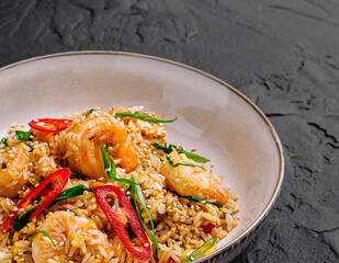 Delicious shrimp fried rice with fresh herbs and chili on a dark background