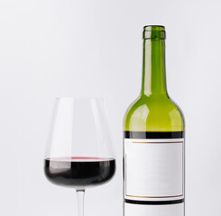 Red wine in a glass beside a bottle on a plain background