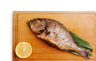 Crispy grilled fish with lemon slice on wooden cutting board