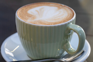 A ribbed ceramic cup filled with frothy cappuccino sits on a matching saucer, topped with heart-shaped latte art.