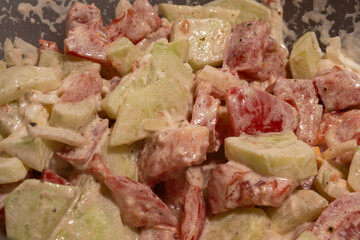 A creamy vegetable salad with cucumbers, tomatoes, and onions is mixed evenly in a rich dressing.