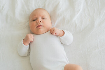 Happy baby. Cute little newborn girl with smiling face lying on bed in bedroom. Infant baby resting playing lying down on white blanket at home. Motherhood happy child childcare concept