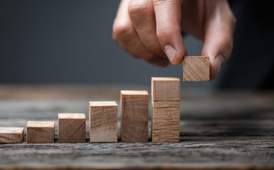 Businessman's hand placing a wooden block on a step, building a structure of success and growth