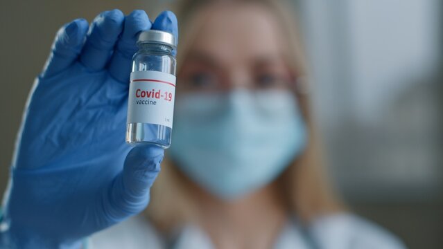 Close-up woman doctor showing vaccine injection bottle in laboratory female scientist nurse girl in medical mask looking at camera holding covid19 coronavirus drug remedy vaccination medicine health - Powered by Adobe