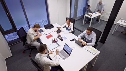 Business coworkers are engaged in a productive meeting, discussing strategies and analyzing data on laptops and documents. The team collaborates efficiently in a modern office environment. - Powered by Adobe