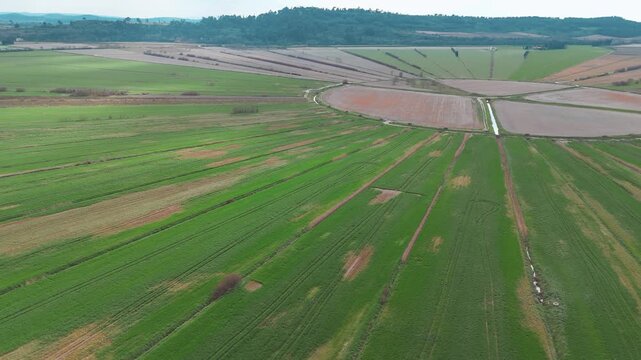 Vue a&eacute;rienne par drone de vastes champs agricoles g&eacute;om&eacute;triques alternant cultures vertes et terre brune avec des traces de machines