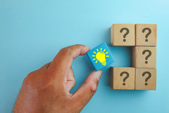 Creative solution and problem solving concept. Hand chooses a lightbulb block among question marks, symbolizing innovation, smart ideas, strategy, and finding the right answer on a blue background.