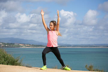 Young girl is doing exercises on cliffs along the ocean