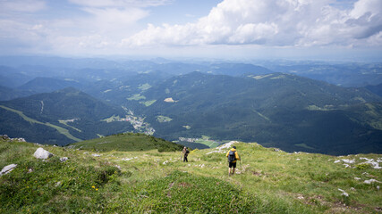 Fototapeta premium Two hikers descending to a valley through green alpine landscape