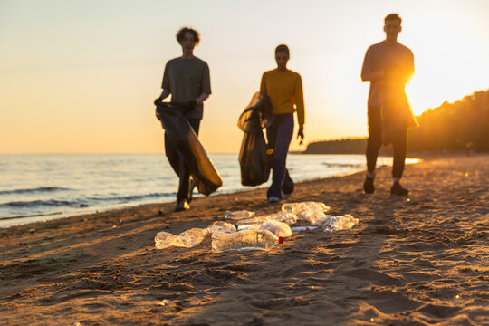 Earth day. Volunteers activists team collects garbage cleaning of beach coastal zone. Woman mans with trash in garbage bag on ocean shore. Environmental conservation coastal zone cleaning
