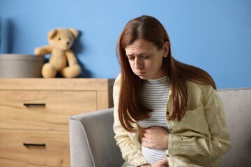 Pregnant woman suffering from nausea in armchair at home. Space for text