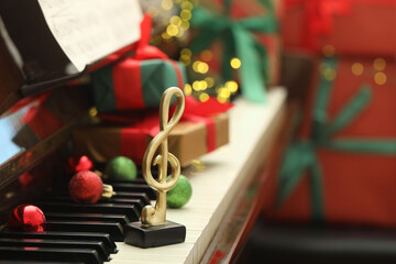 Christmas atmosphere. Golden treble clef, baubles and gift boxes on piano, closeup with space for text. Bokeh effect