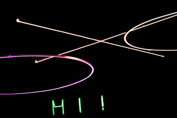 abstract composition featuring bright neon light rings and linear elements in pink, yellow, and white against a dark background. below the installation, green and red illuminated letters word hi