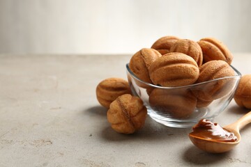 Delicious nut shaped cookies with boiled condensed milk and spoon on light textured table, closeup. Space for text