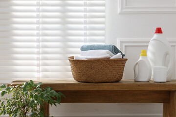 Laundry basket with clean clothes and detergents on wooden bench near window indoors