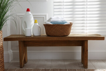 Laundry basket with clean clothes and detergents on wooden bench near window indoors