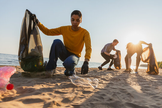Earth day. Volunteers activists team collects garbage cleaning of beach coastal zone. Woman mans puts plastic trash in garbage bag on ocean shore. Environmental conservation coastal zone cleaning