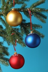 Christmas balls hanging on fir tree branches against light blue background, closeup