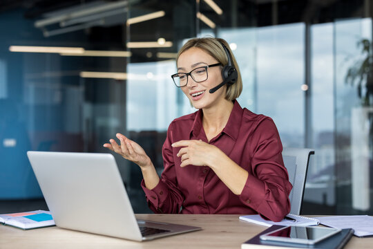Young businesswoman wearing a headset while actively participating in a video call on her laptop, communicating with clients or team members from a modern office setting