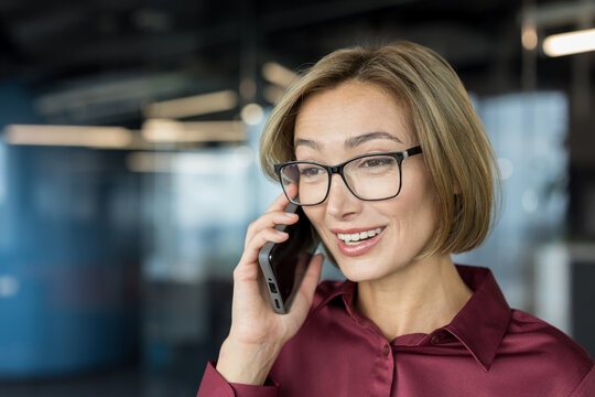 Female professional conducting a business conversation on a mobile phone, smiling while communicating and networking with clients or colleagues in a corporate setting