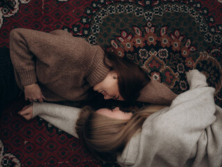 Happy lesbian couple lying ornate carpet facing smiling looking eyes
